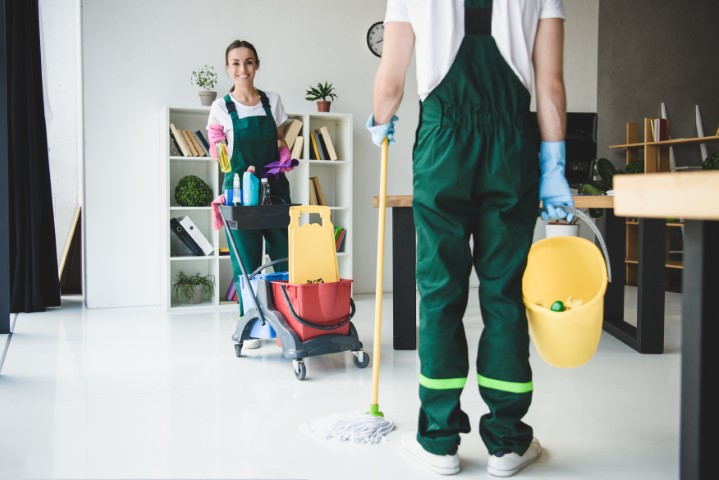 Woman and man cleaning and office with mops